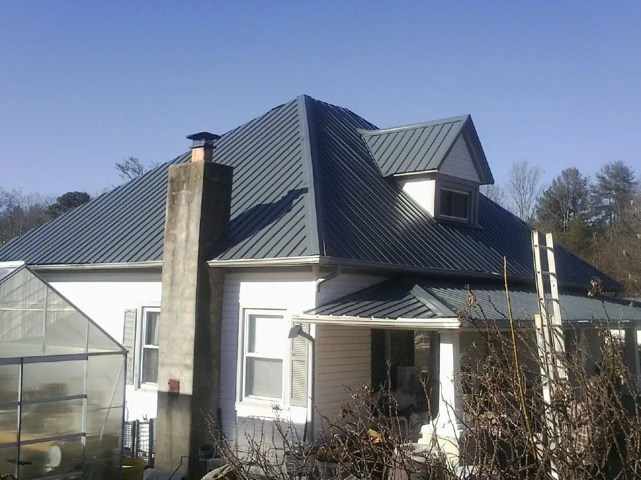 Dark blue standing seam metal roof on a white farmhouse with dormer — Slate & Tile Roof Repair by Roofing Brothers in South Charleston