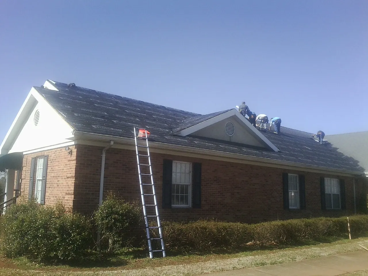 Crew tearing shingles off a brick ranch roof with a ladder set — Metal Roof Repair work by our crew in South Charleston