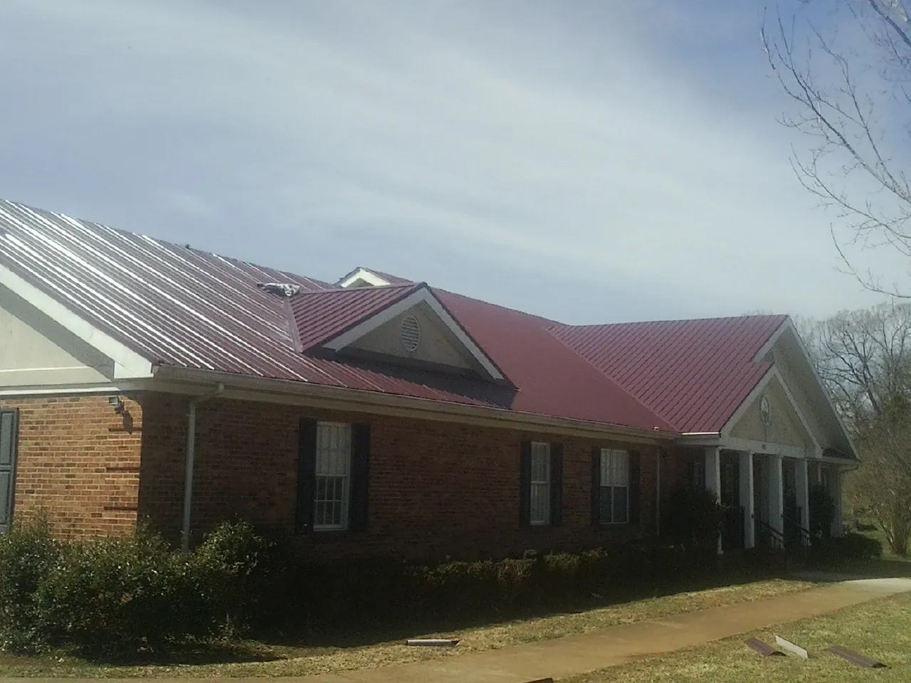 Red metal roof with gabled entries on a long brick building, from a Hail Damage Roof Repair job in South Charleston