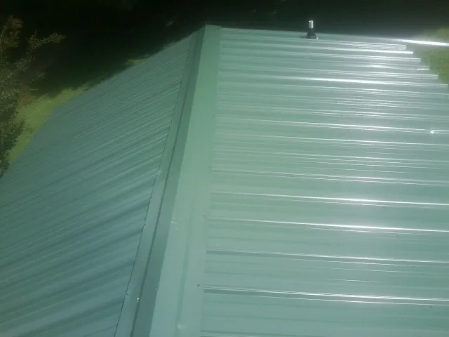 New green metal panels meeting at the ridge of a roof — Flat Roof Repair work by our crew in South Charleston