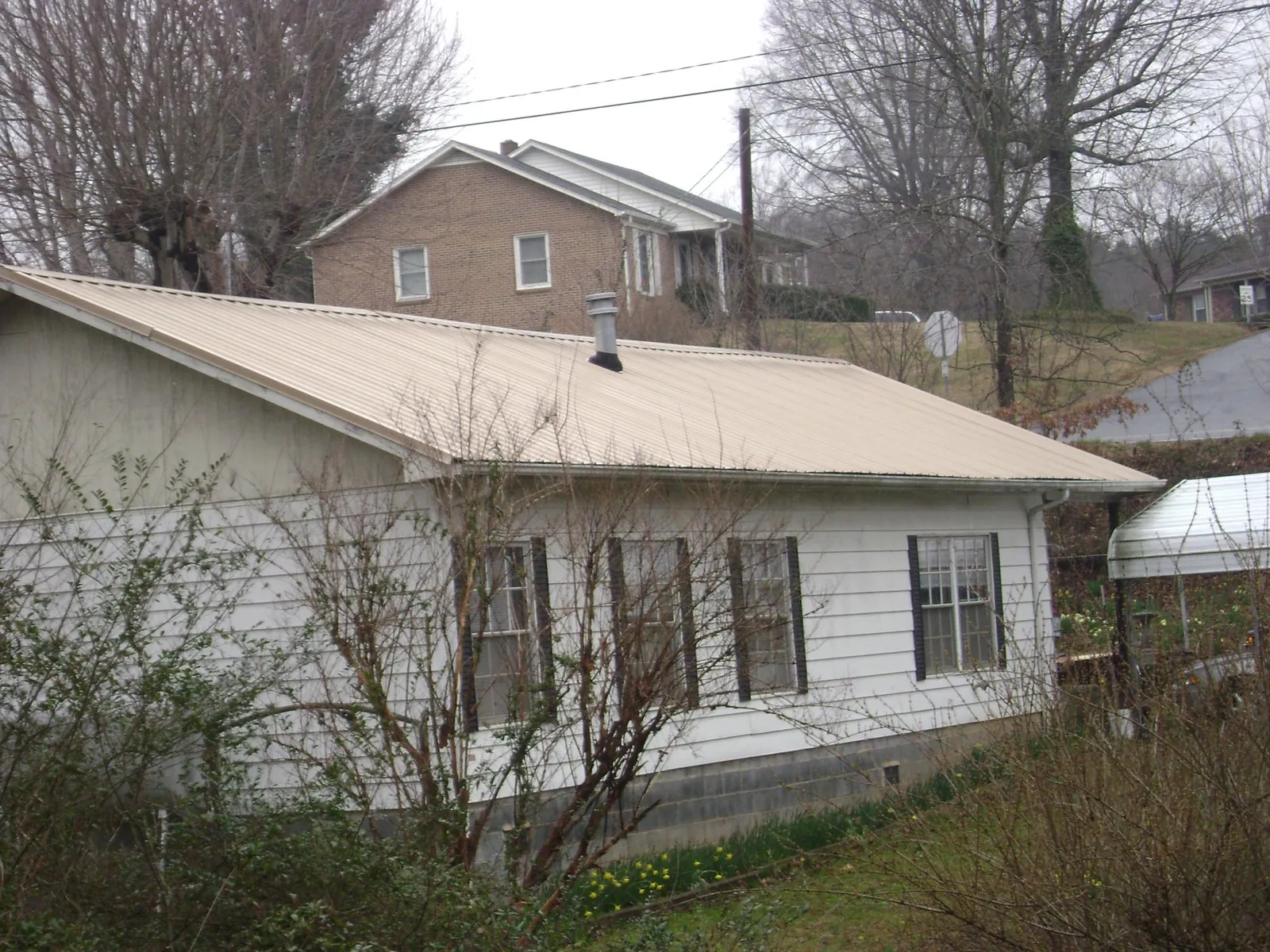 Tan metal roof on a white sided house set into a hillside — Commercial Roofing by Roofing Brothers in South Charleston